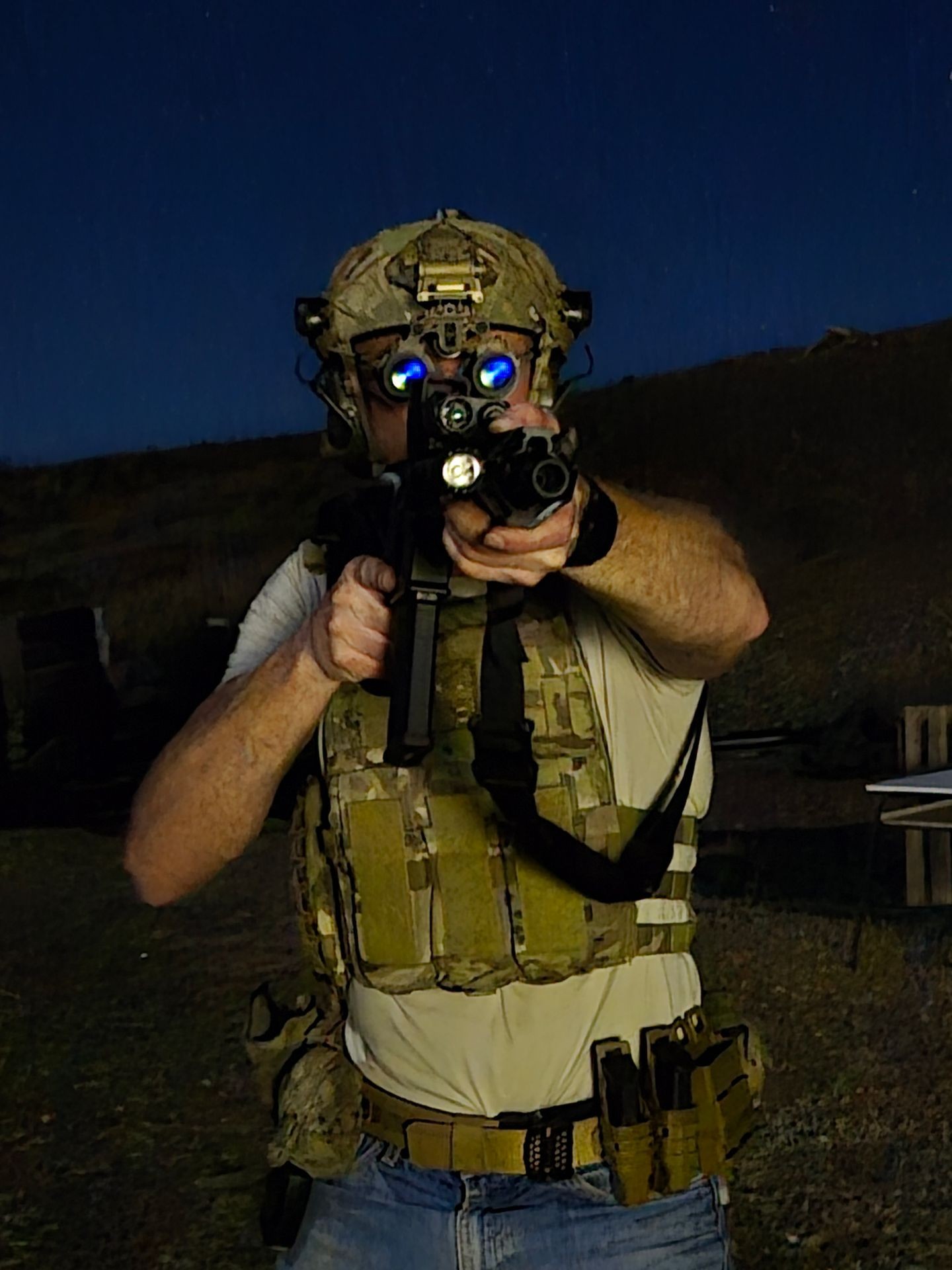 Person in tactical gear aiming a rifle at night, wearing a helmet with night vision goggles.