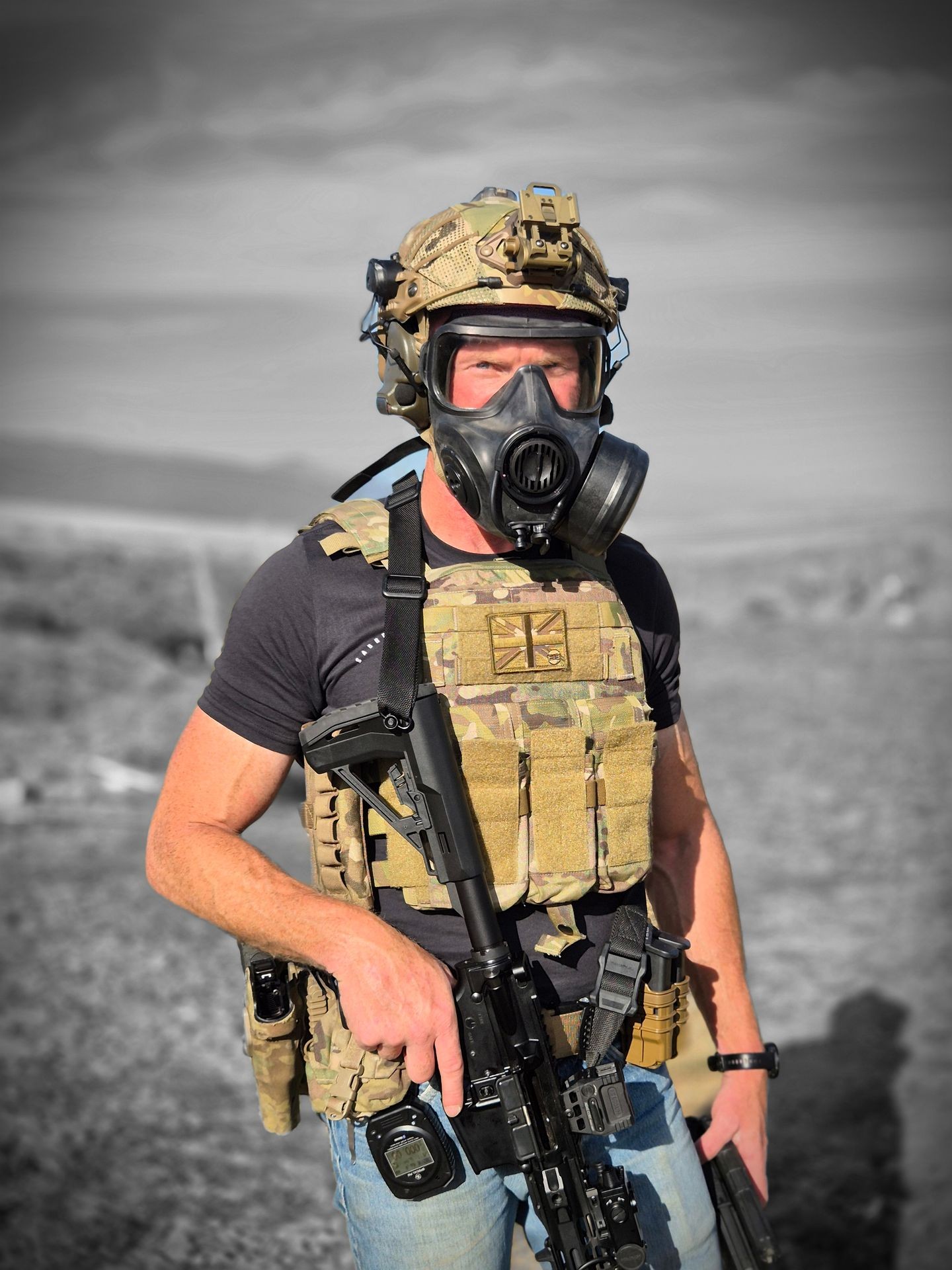 Person in tactical gear and gas mask holding a rifle in a grayscale outdoor setting.